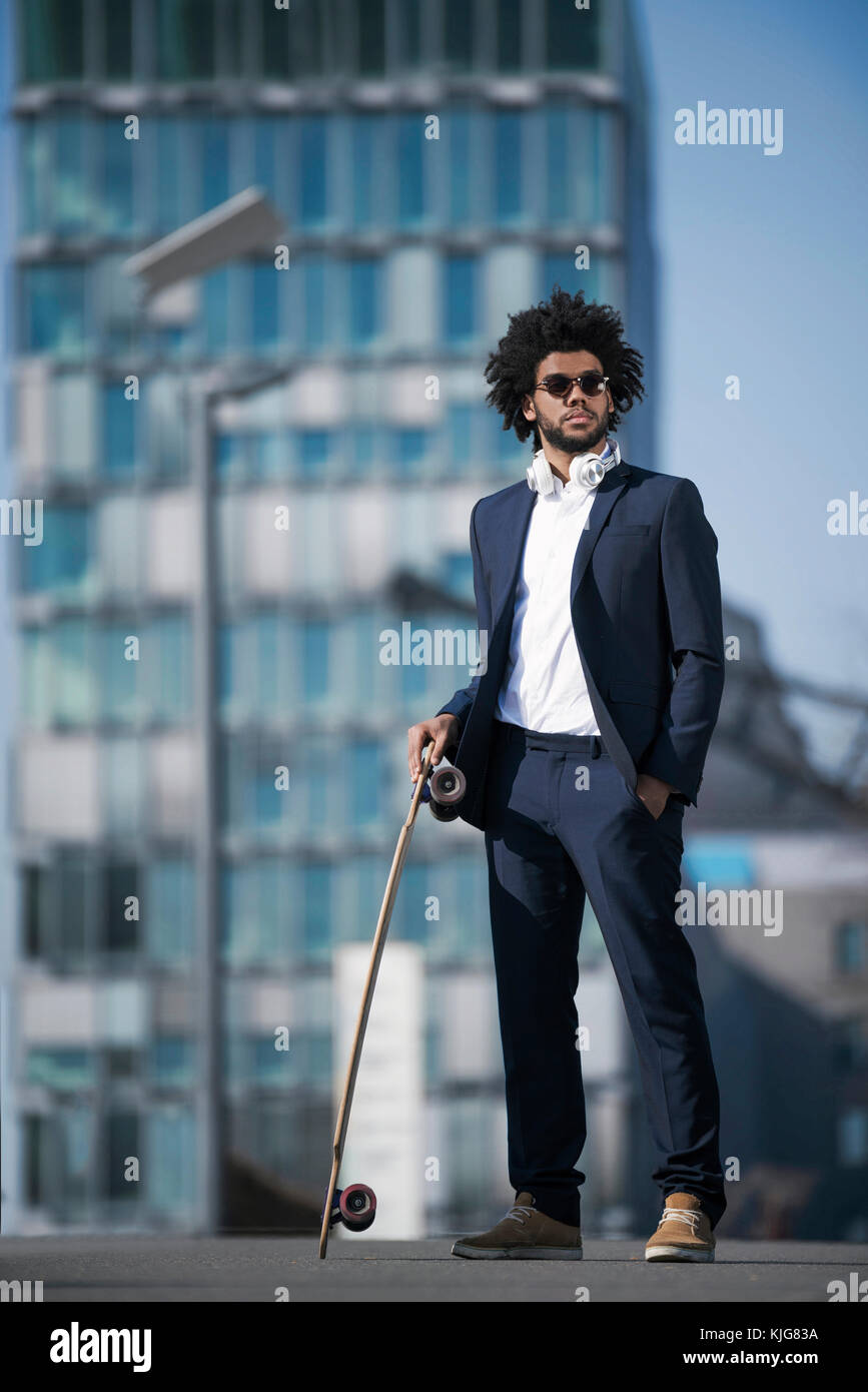 Businessman with longboard standing in front of skyscraper Banque D'Images Businessman with longboard standing in front of skyscraper Banque D'Images