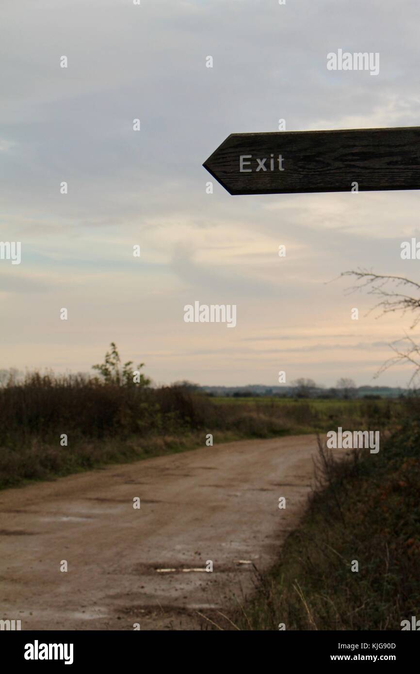 Enseigne de sortie en bois au crépuscule pointant vers la gauche avec chemin de terre allant dans la distance Banque D'Images