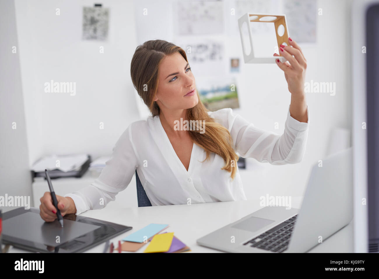 Young woman at desk in office holding model et à l'aide de tablette graphique Banque D'Images