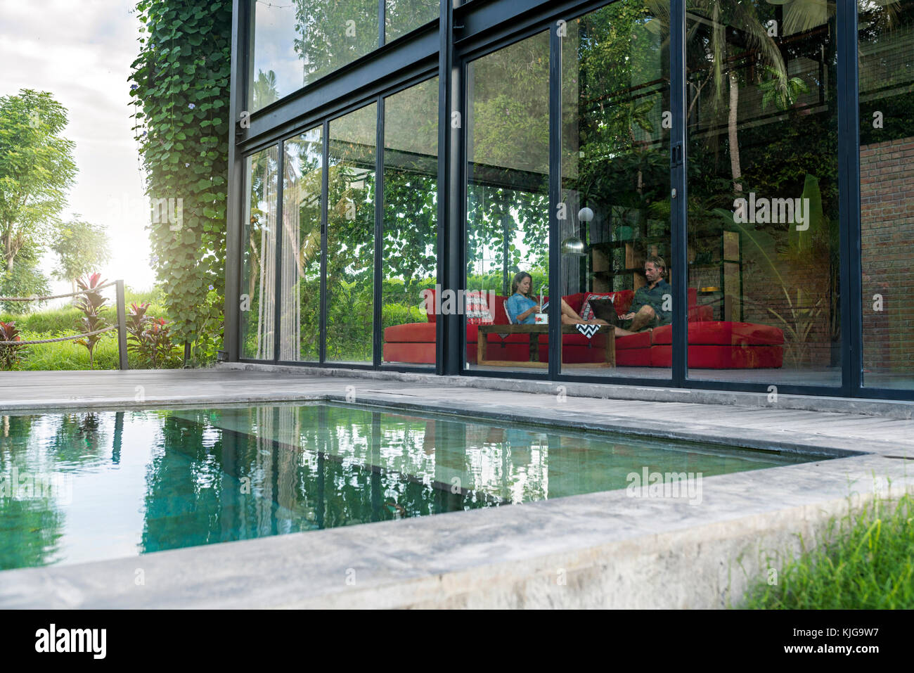 Sur le jardin grâce à façade en verre de couple avec ordinateur portable et réserver des sur la table rouge de conception moderne maison en face de la piscine Banque D'Images