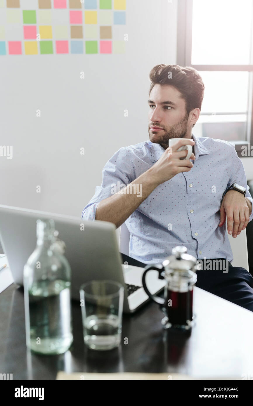 Young businessman sitting at desk with pot de café Banque D'Images