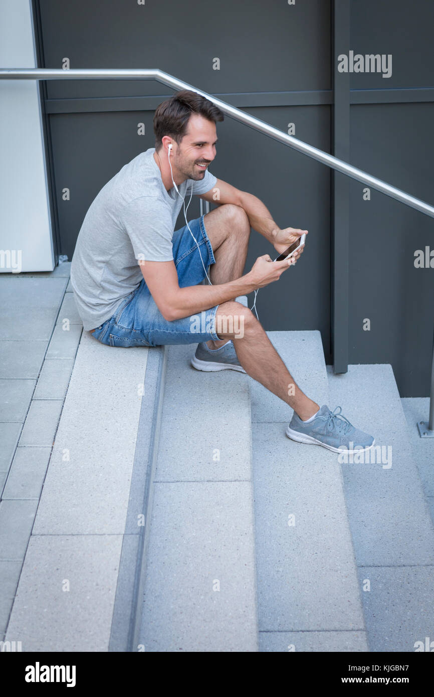 Homme assis sur les escaliers, using smartphone Banque D'Images