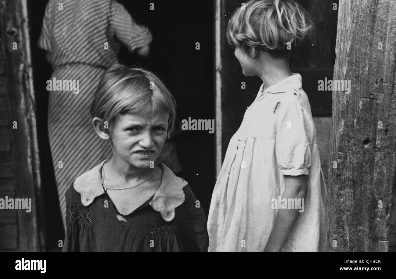 Une photographie de deux jeunes filles qui sont des enfants d'un fermier, ils portent des vêtements simples qui montre des signes d'usure, leur mère peut être vu par la porte à l'arrière-plan, elle porte une robe avec des taches visibles, plaquemines parois, Louisiane, 1935. à partir de la bibliothèque publique de new york. Banque D'Images