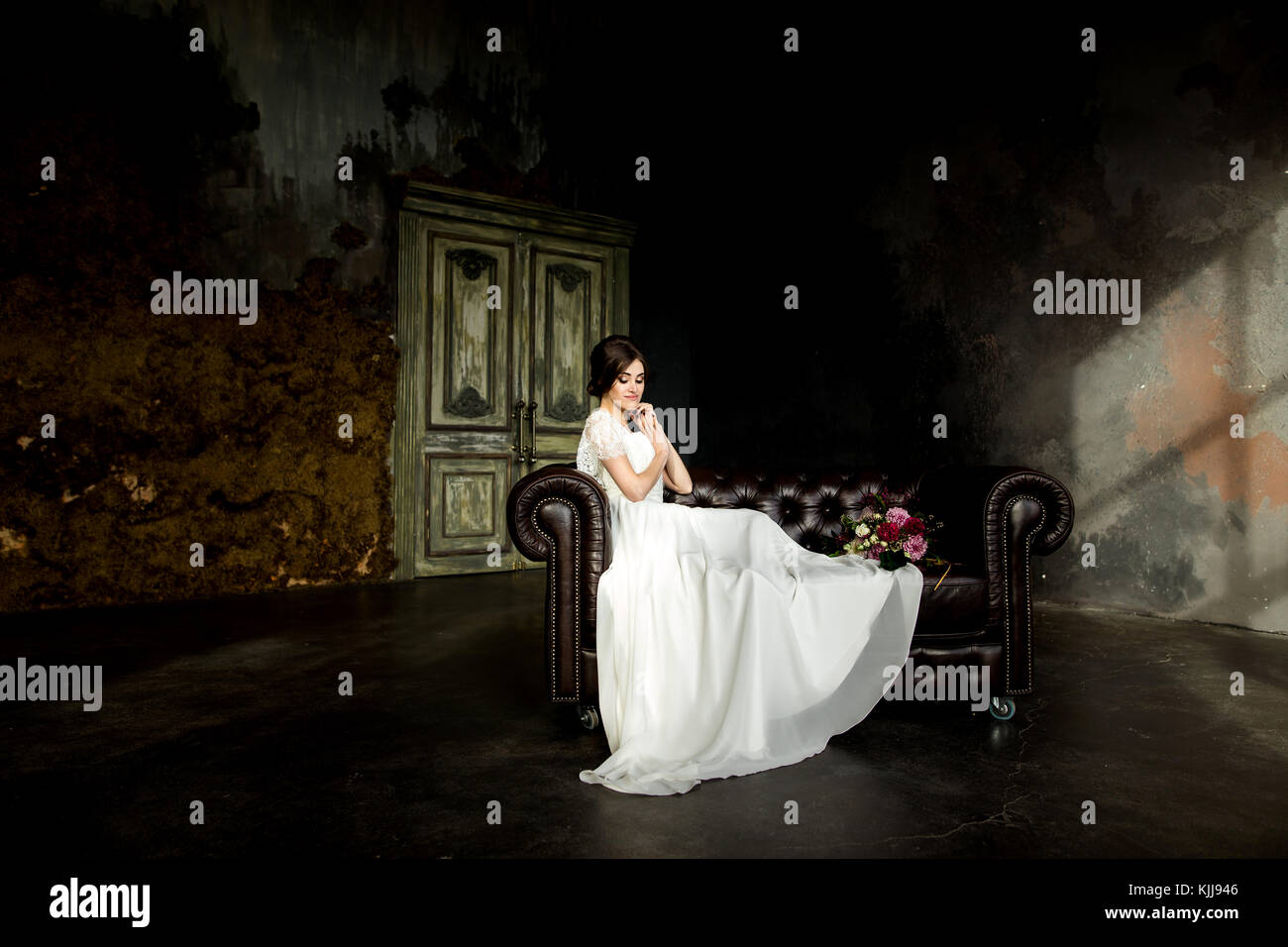 Belle robe de mariée assis sur une chaise à l'intérieur dans dark studio intérieur comme à la maison. Banque D'Images