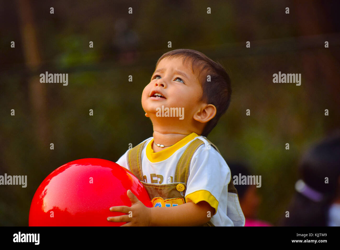 Mignon bébé jouant avec une boule rouge dans le jardin, Pune, Maharashtra. Banque D'Images