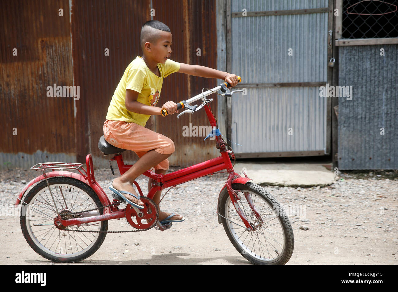 Boy riding a bike dans un bidonville. Battambang. Le Cambodge. Banque D'Images