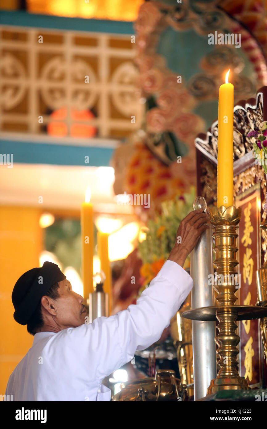 Saint-siège Caodai Temple. Bougie d'éclairage prêtre sur l'autel pendant 12 heures rituel. Thay Ninh. Le Vietnam. Banque D'Images