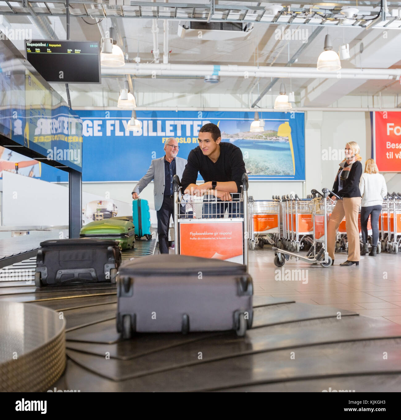 Jeune homme avec chariot en attente de ses bagages de l'aéroport à la courroie du convoyeur Banque D'Images