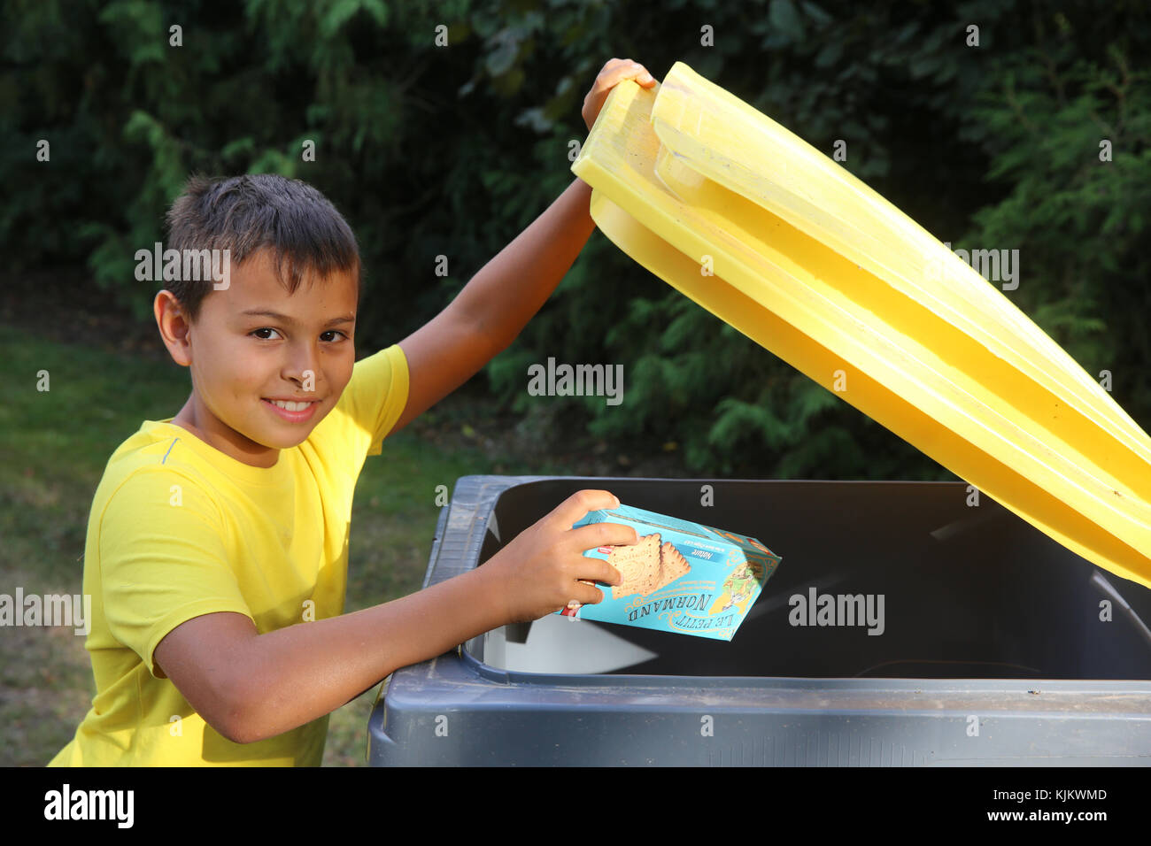 Garçon en train de lancer une boîte dans une poubelle de recyclage. La France. Banque D'Images
