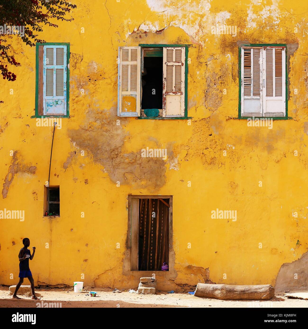 Un garçon solitaire marchant devant un grand mur jaune dans une rue de l'île de Gorée au Sénégal Banque D'Images