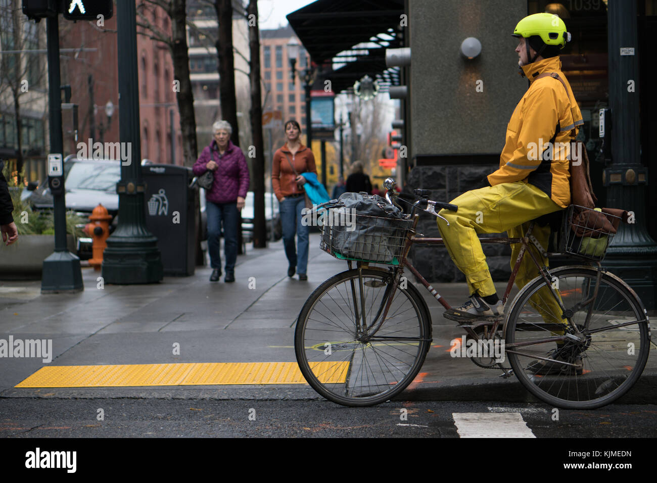 22 novembre 2017 - Portland OU. Un homme est assis sur un vieux vélo sale avec des paniers holding sacs, portant des vêtements de pluie vélo jaune en milieu urbain. Banque D'Images