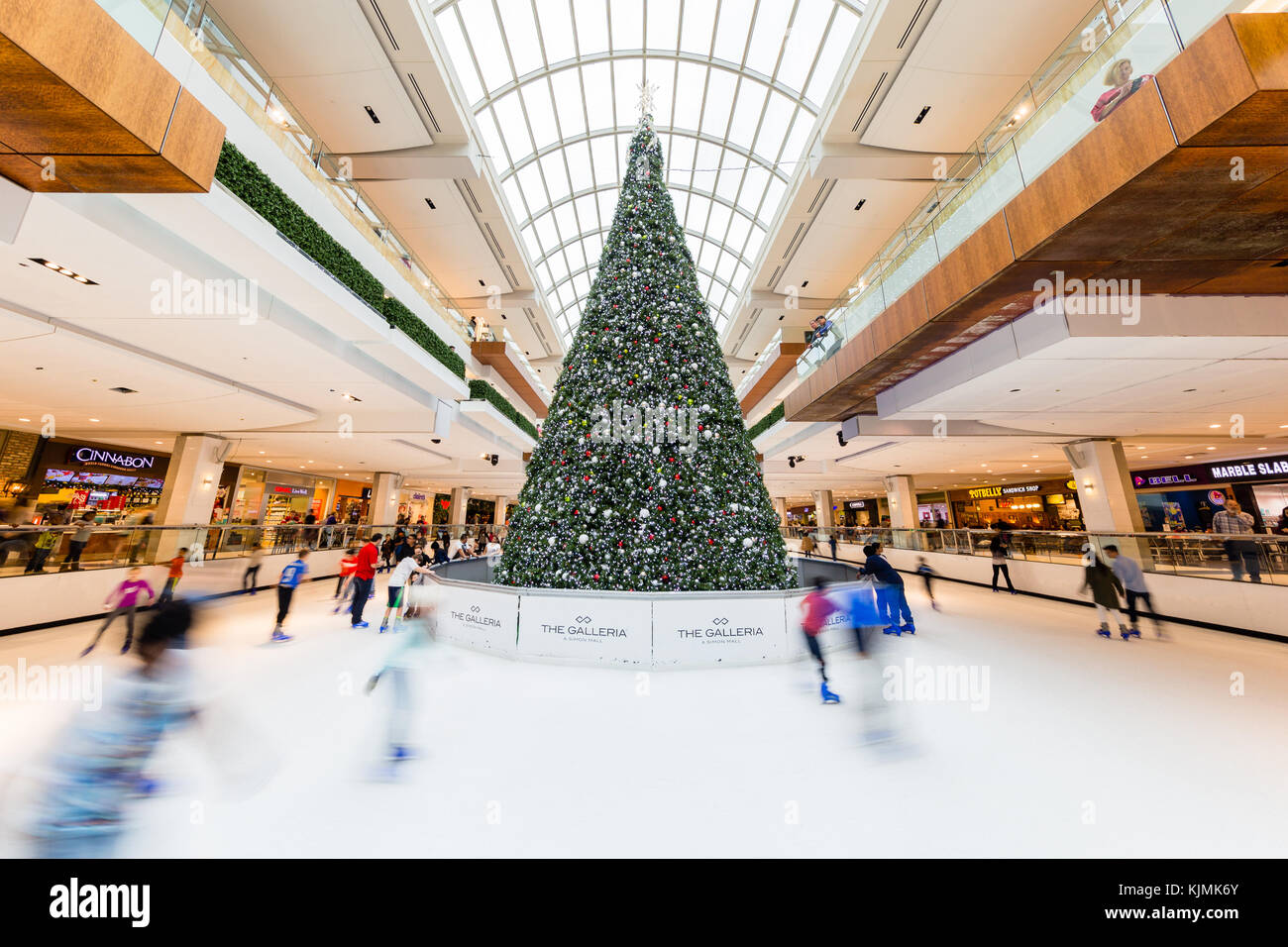 Les enfants et les jeunes adultes patinage autour d'arbre de Noël dans la patinoire de patinage dans une grande galerie marchande couverte Banque D'Images