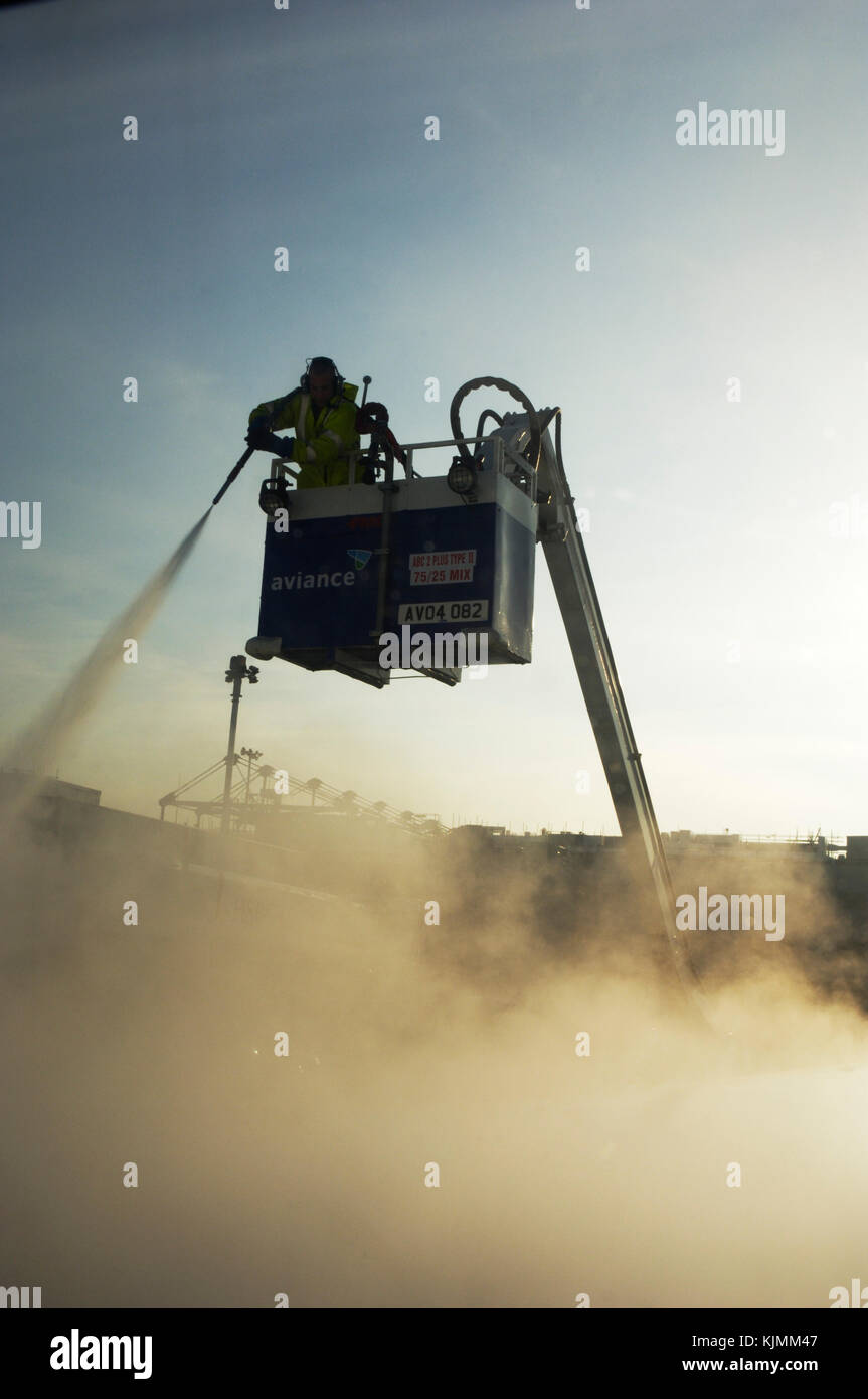Un homme debout sur une plate forme élévatrice, la pulvérisation du liquide de dégivrage sur une aile d'avion tôt le matin avant l'avion peut décoller. L'hiver. Banque D'Images