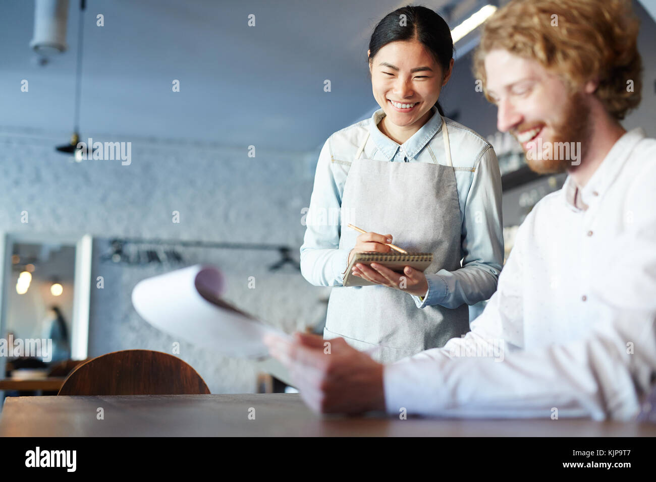 Serveuse asiatique de rire tandis que jeune homme choisir quelque chose à manger à partir de menu Banque D'Images