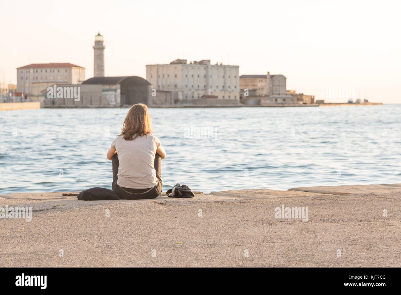 Une jeune femme solitaire vu de dos est assis au bord d'une marina à Trieste, Italie Banque D'Images