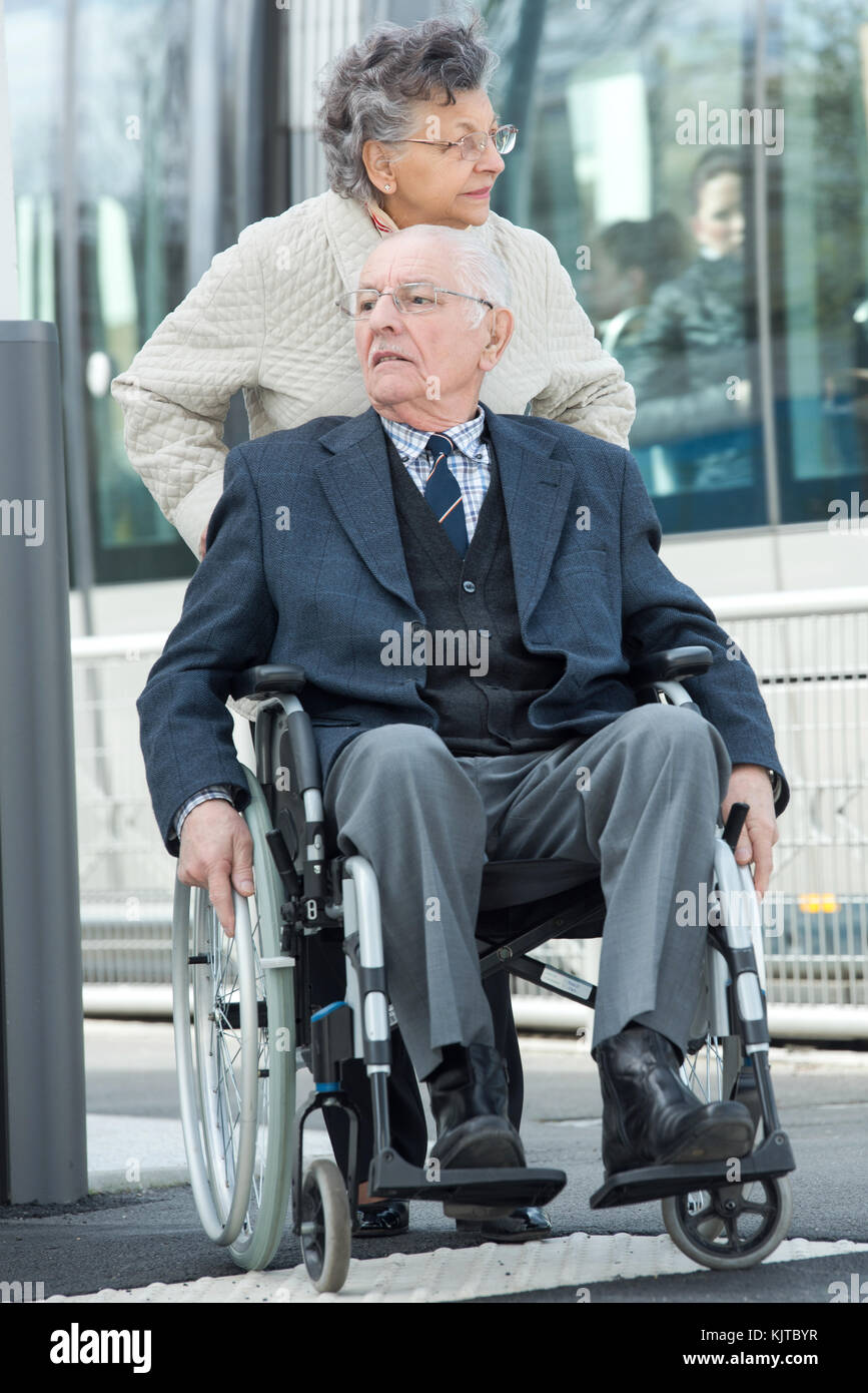 Un homme âgé assis en fauteuil roulant poussé par son épouse Banque D'Images