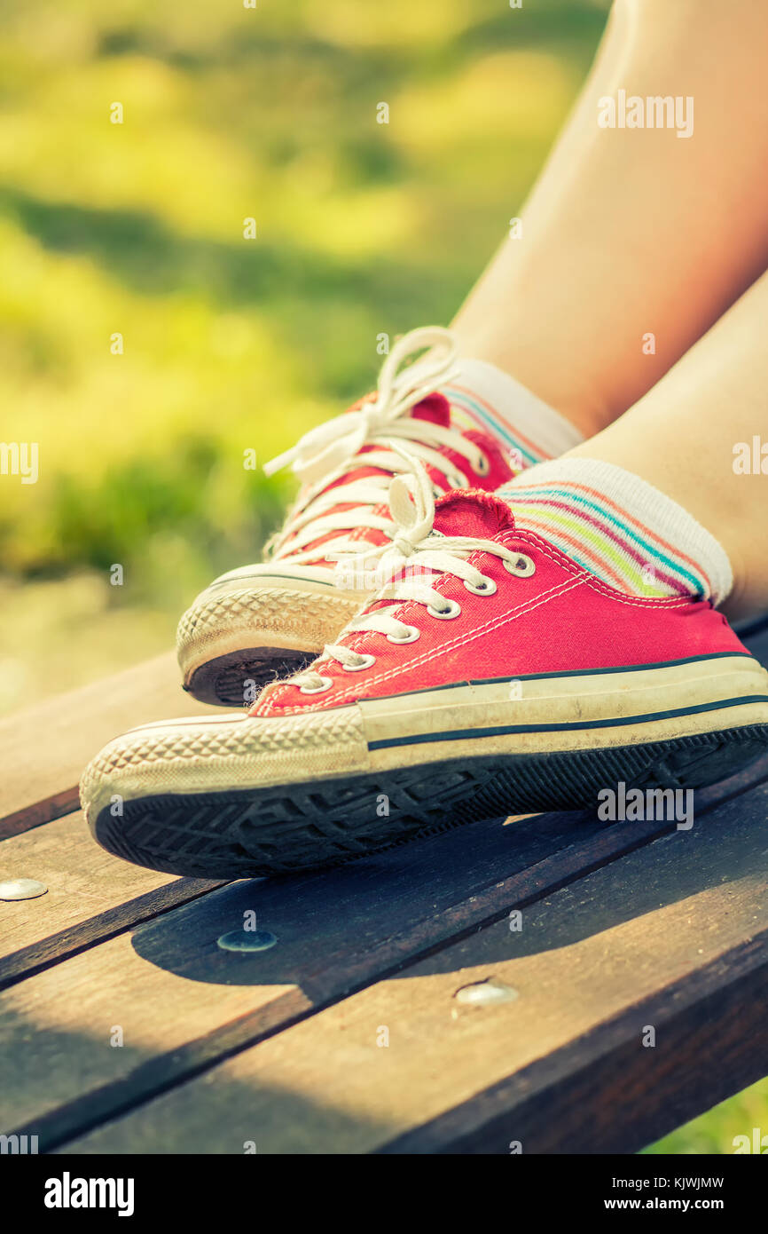 Pieds de femme dans un rouge lumineux toile sneakers assis sur un banc Banque D'Images