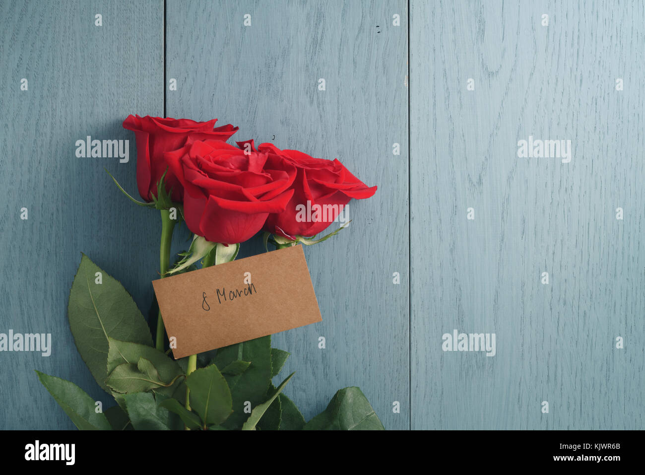 Trois roses rouges sur la table en bois bleu avec 8 carte papier mars Banque D'Images