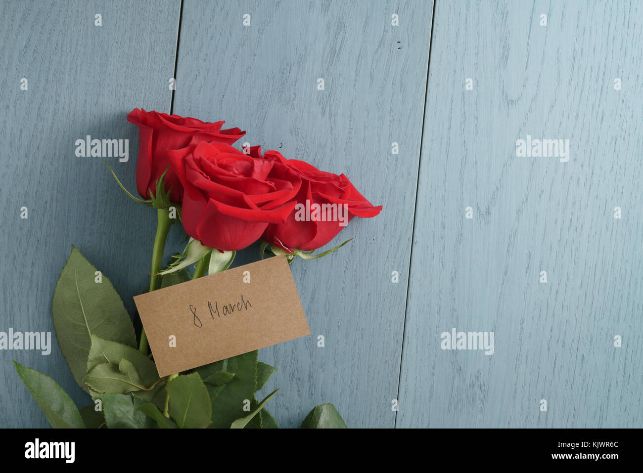 Trois roses rouges sur la table en bois bleu avec 8 carte papier mars Banque D'Images
