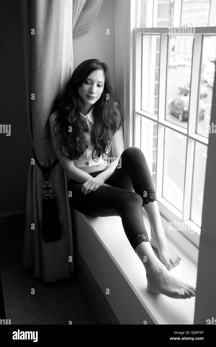 Belle fille brune aux cheveux longs assis par une fenêtre Banque D'Images