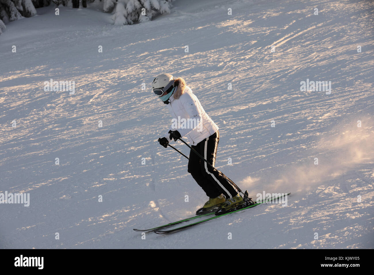 Skieur dans combinaisons blanches avec le casque blanc sur la tête des  manèges sur les pentes. la pente de ski sur une colline, des arbres  couverts de neige baignée d'une golden sunse