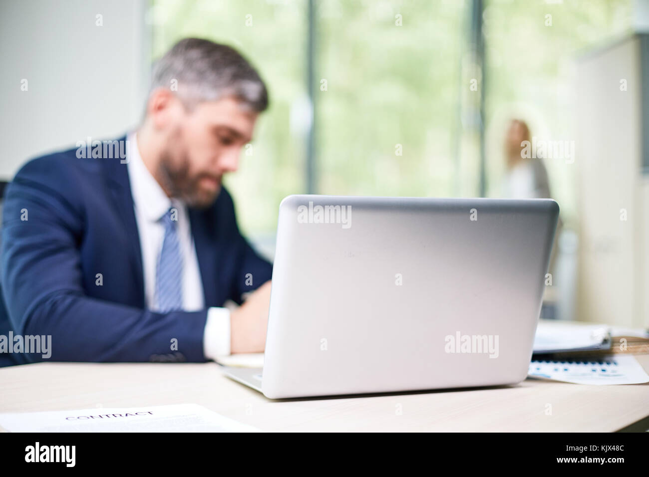 Open plan office occupé : gestionnaire d'âge moyen enveloppé dans travailler assis à 24 pendant que son collègue debout à la fenêtre panoramique Banque D'Images