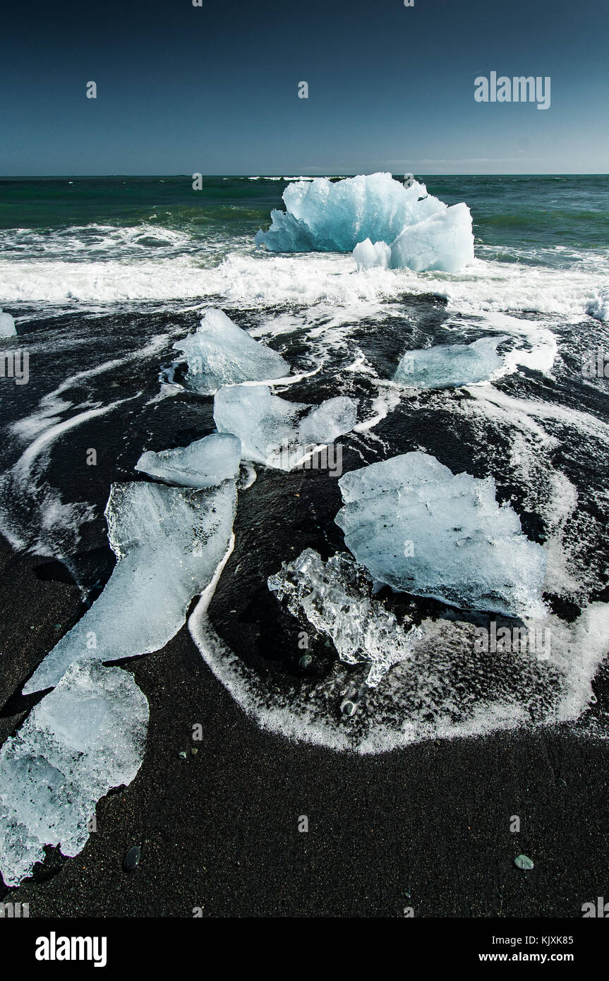 Les vagues de l'océan, jouer avec les blocs de glace rejetée sur la plage volcanique noire près de l'Islande Jökulsárlón Banque D'Images