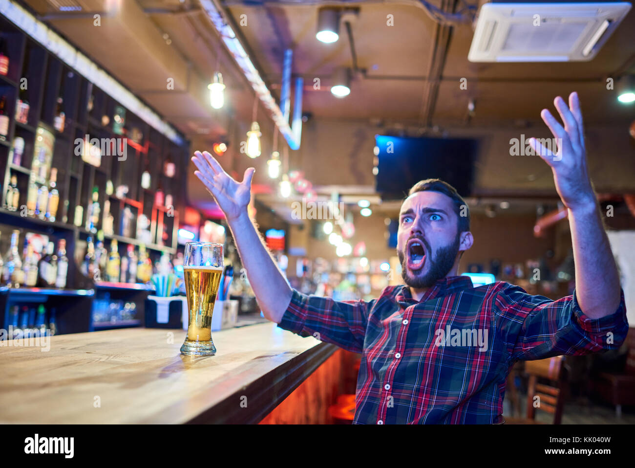 Portrait de phoque barbu fan de sport cheering émotionnellement dans pub regarder match à la télévision assis au comptoir du bar avec les mains levées dans l'étonnement, copy space Banque D'Images