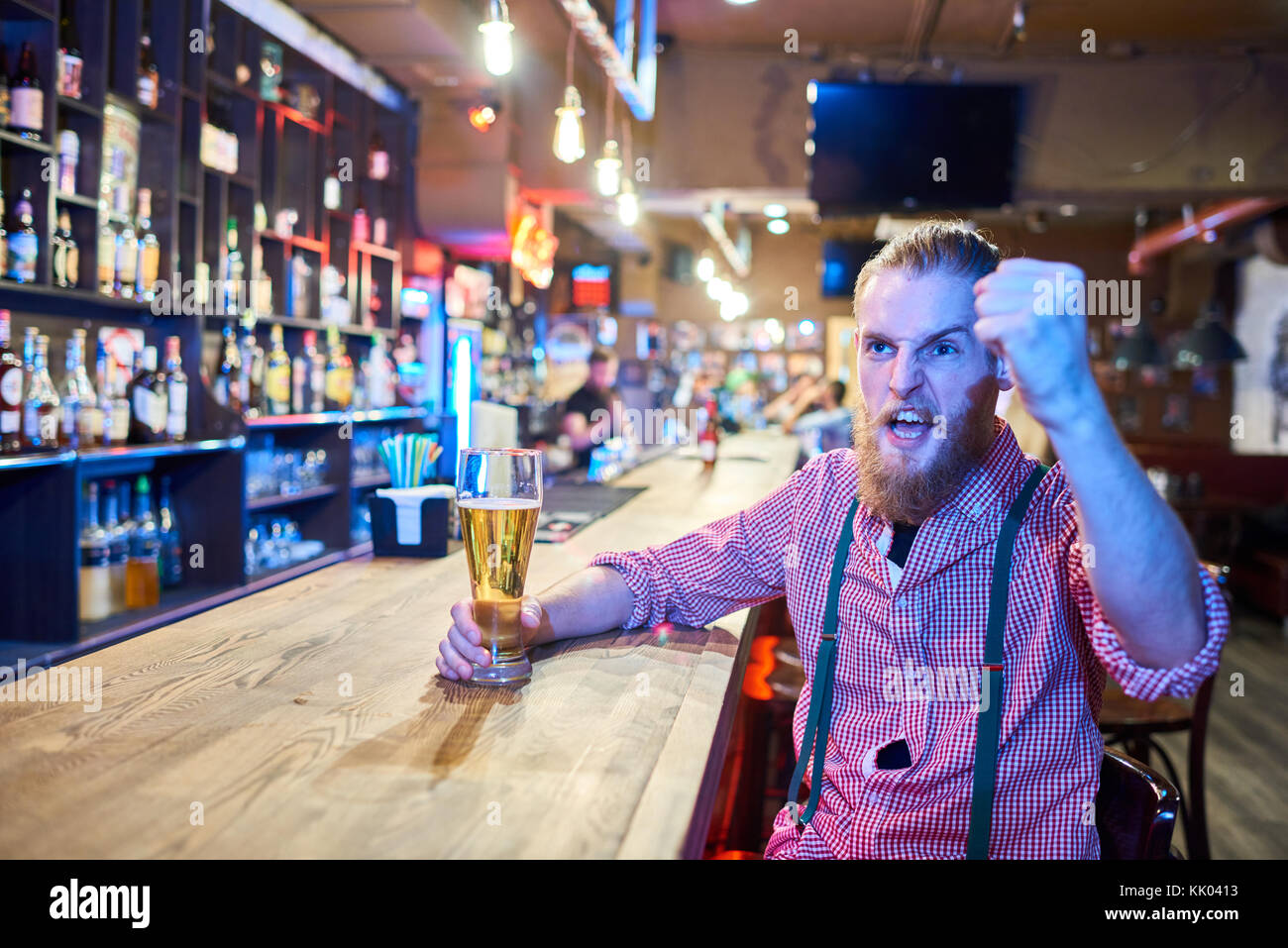 Portrait d'homme barbu émotionnel tout en acclamant les sports, match à la télévision assis au comptoir de pub avec grand verre de bière, copy space Banque D'Images