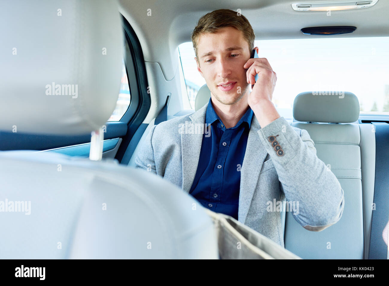 Portrait de jeune homme parlant par téléphone assis sur siège arrière de voiture de luxe, copy space Banque D'Images