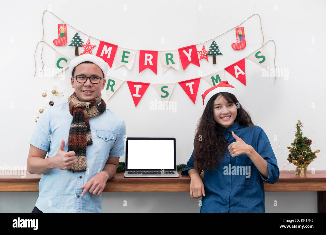 Smiling couple amoureux à Noël d'un drapeau bunting et Thumbs up with avec coffre,modèle mokc écran blanc ordinateur pour l'affichage du design,ho Banque D'Images