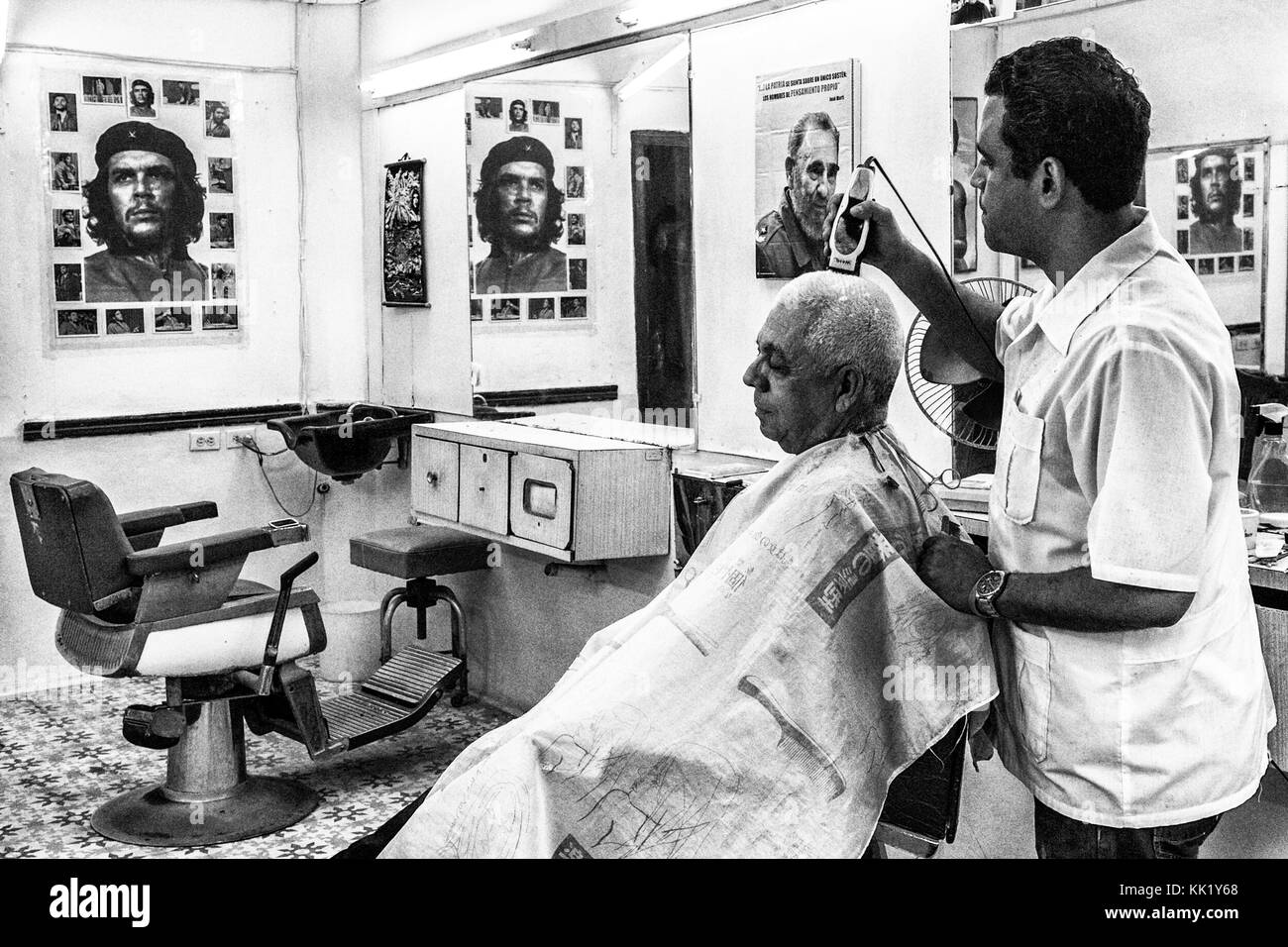 Une coiffure couper les poils à un client avec le rasoir électrique dans un magasin rempli d'affiches révolutionnaires, Vieille Havane, Cuba Banque D'Images