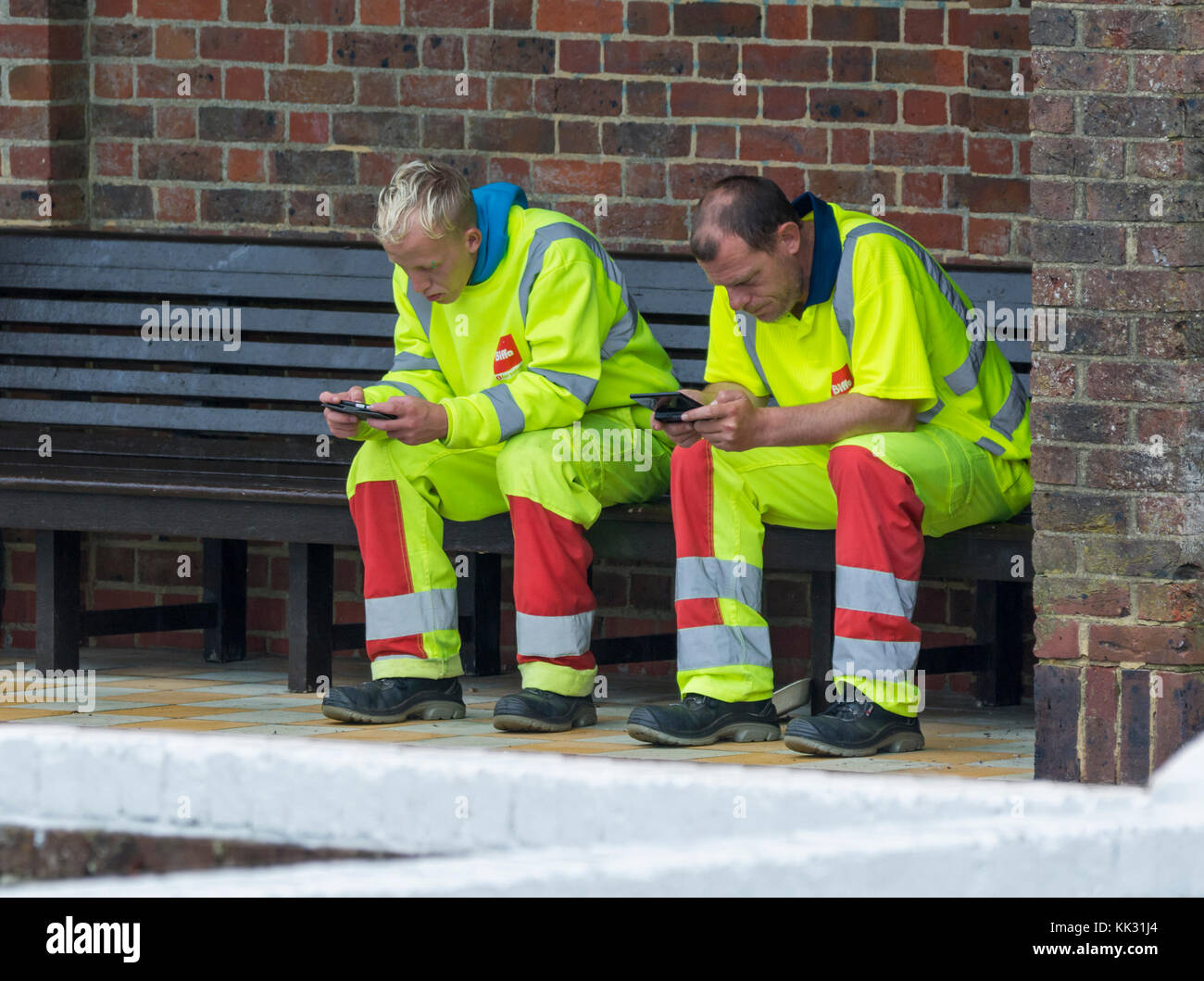 Paire d'ouvriers hommes assis en faisant une pause pendant l'utilisation de téléphones mobiles. Banque D'Images
