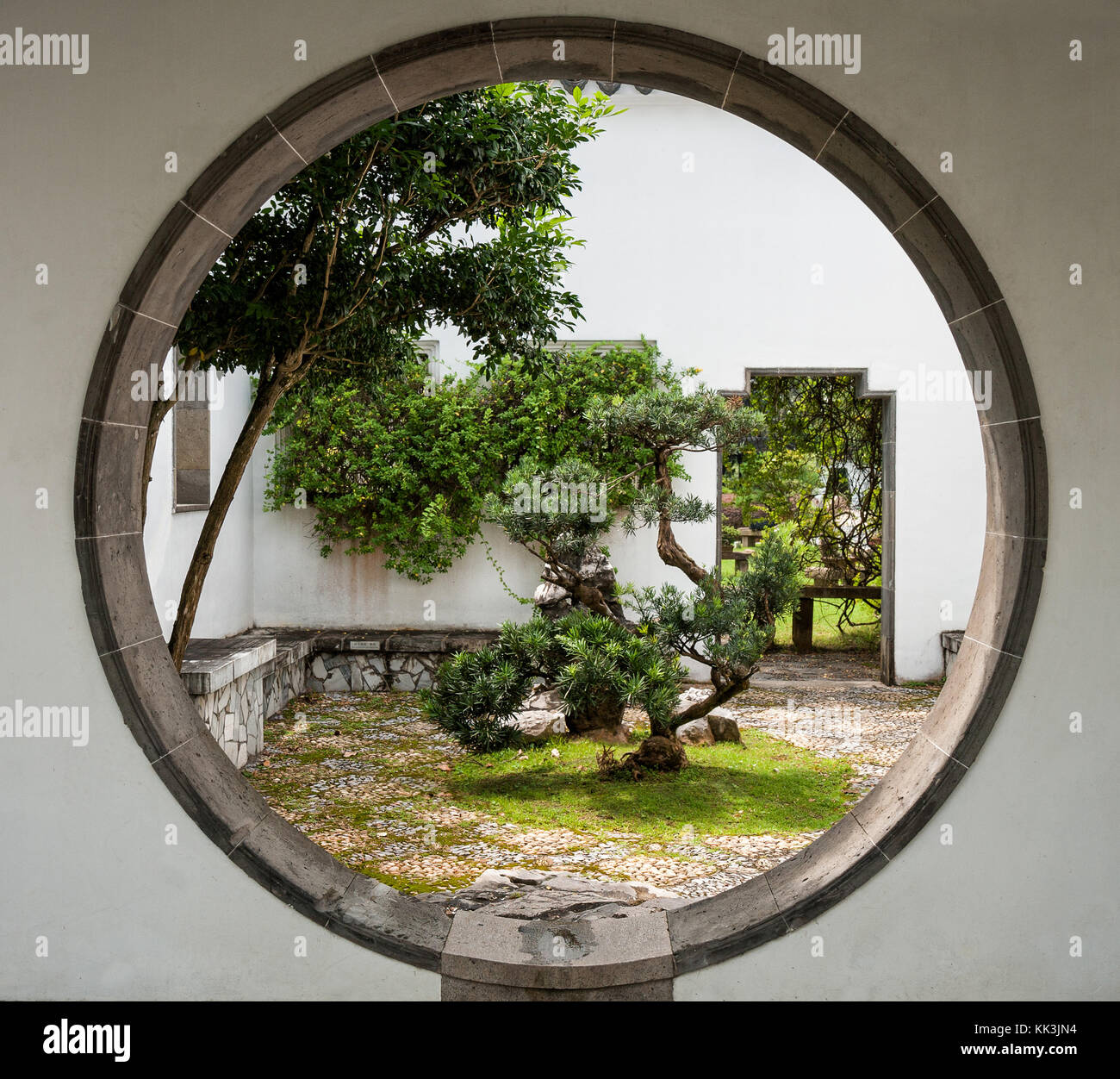 Singapour, jardin bonsai chinois. mur avec un trou circulaire entre les chantiers Banque D'Images