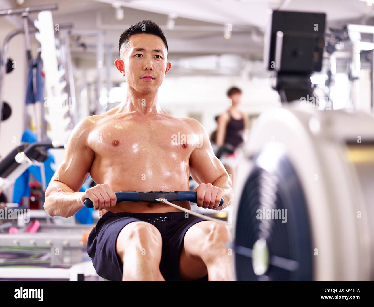 Jeune homme travaillant sur le muscle d'Asie en salle de sport à l'aide d'une machine à ramer. Banque D'Images