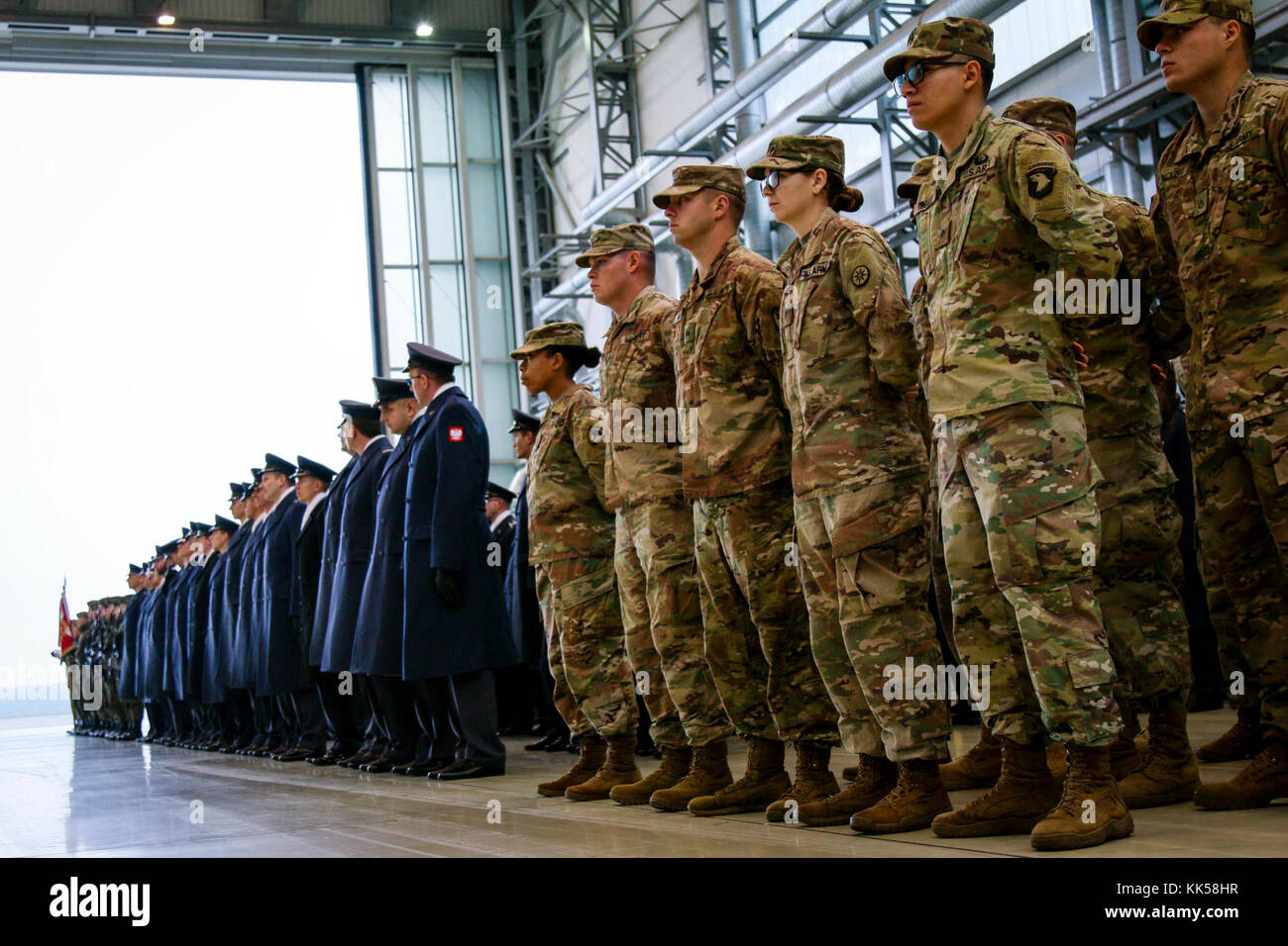 Les soldats de l'armée américaine (à droite, en vert) et les aviateurs polonais (à gauche, en bleu) avec la 3e Airlift Wing attendre pour commencer une cérémonie de promotion de l'armée polonaise à Powidz, Pologne, le 10 novembre 2017. Les soldats américains sont déployés dans le cadre de l'Atlantic résoudre, une entreprise américaine de s'acquitter des engagements de l'OTAN par rotation des unités dans l'ensemble du théâtre européen à prévenir les agressions contre les alliés de l'OTAN en Europe. (U.S. Photo de l'armée par la CPS. Hubert D. Delany III/22e Détachement des affaires publiques mobiles) Banque D'Images