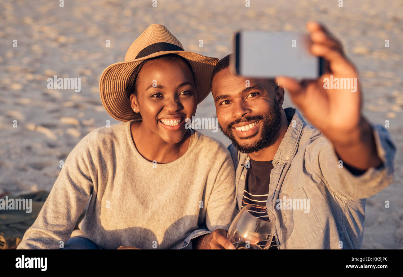 Happy young couple en tenant vos autoportraits ensemble à la plage Banque D'Images