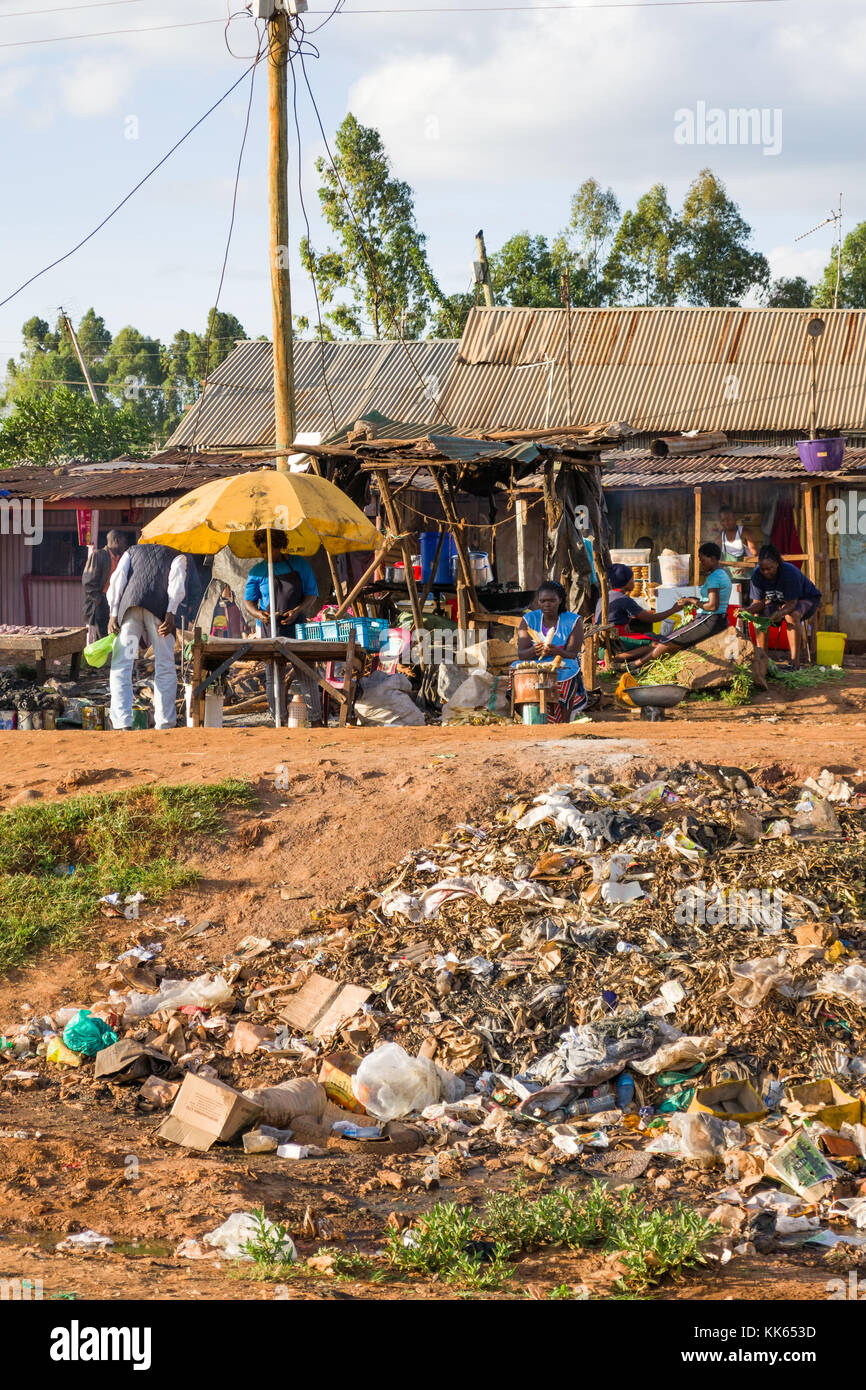 Détritus éparpillés sur le sol en face de gens allant de la vie quotidienne dans des taudis Githogoro, boutiques et des baraques ainsi que les stalles en arrière-plan, au Kenya Banque D'Images