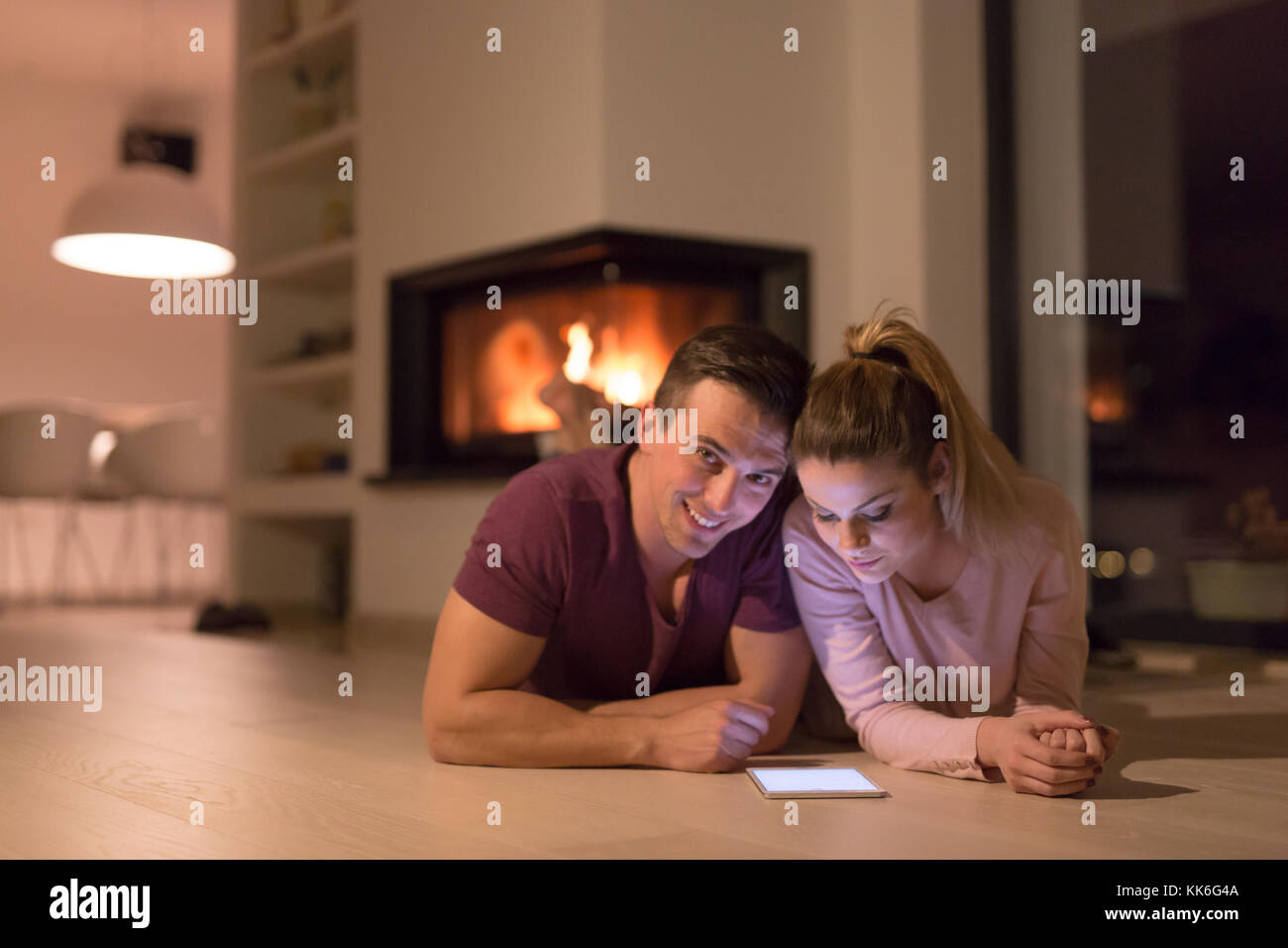 Jeune couple sur le sol en face de cheminée internet surf using digital tablet on nuit froide d'hiver Banque D'Images