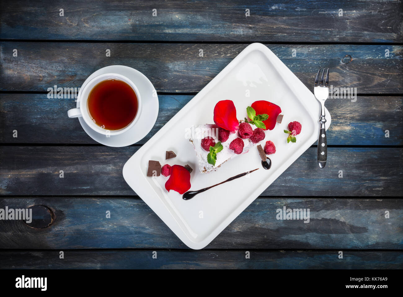 Délicieux pavlova gâteau avec une tasse de thé. de framboises fraîches sur une plaque blanche avec des pétales de rose. vue d'en haut. Beau fond de bois. Banque D'Images