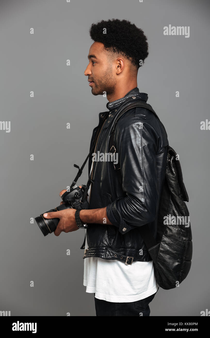 Vue latérale photo de beau sac à dos élégant homme africain avec holding photo appareil photo, isolé sur fond gris Banque D'Images