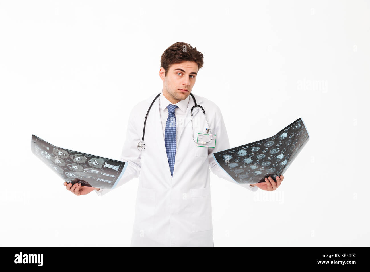 Portrait d'un jeune homme confus doctor with stethoscope habillés en uniforme holding x-ray en haussant les épaules et des photographies plus isolé bac blanc Banque D'Images