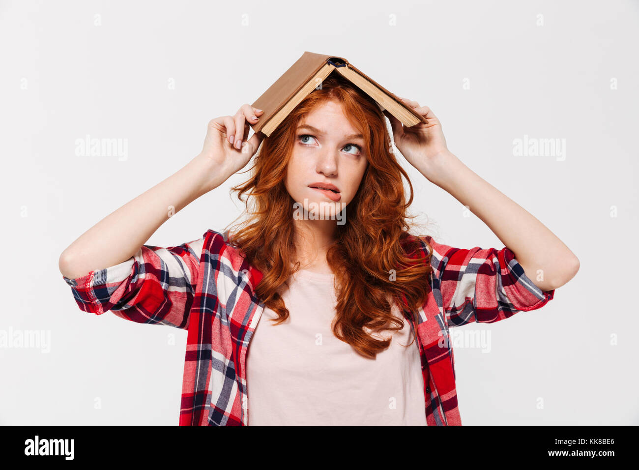 Pensive woman in gingembre shirt holding livre sur la tête comme toit et à la recherche sur fond gris Banque D'Images