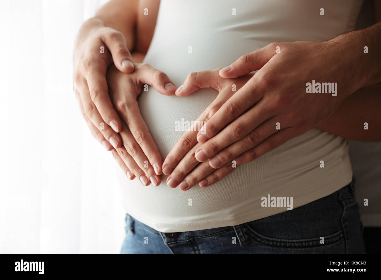 Close up portrait of man's woman's hands et faisant des gestes du cœur sur l'intérieur du ventre enceinte Banque D'Images