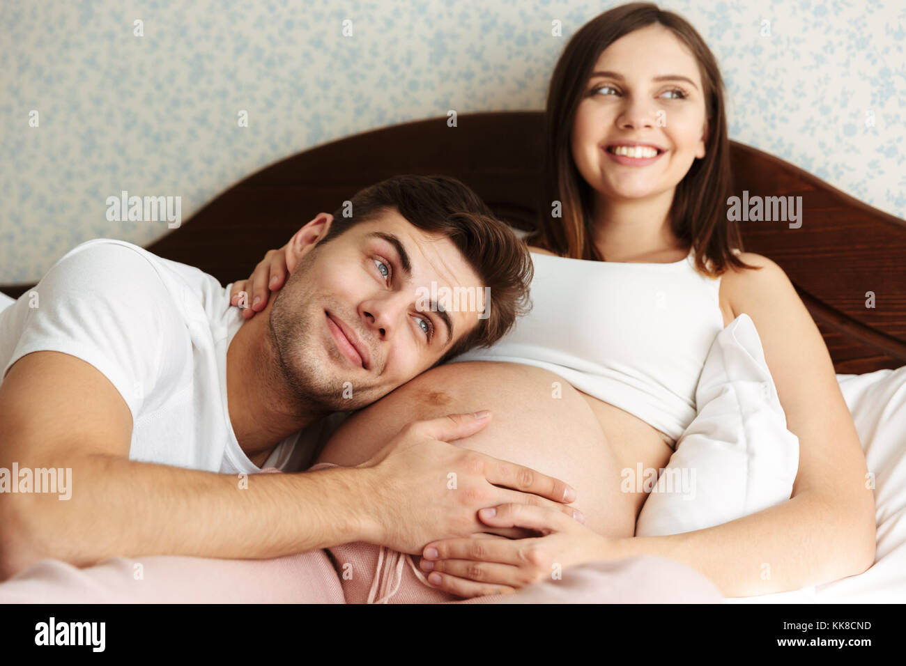 Jeune femme enceinte au lit avec son mari dans la chambre à coucher,  l'homme est allongé sur son ventre Photo Stock - Alamy