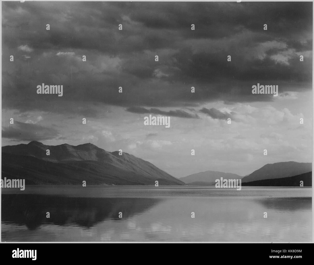 Photographie noir et blanc, à la recherche de l'autre côté du lac de montagnes et nuages, titré "Soirée, McDonald Lake, Glacier National Park', par Ansel Adams, à partir de photographies des Parcs Nationaux et Monuments, Montana, United States, 1941. Banque D'Images