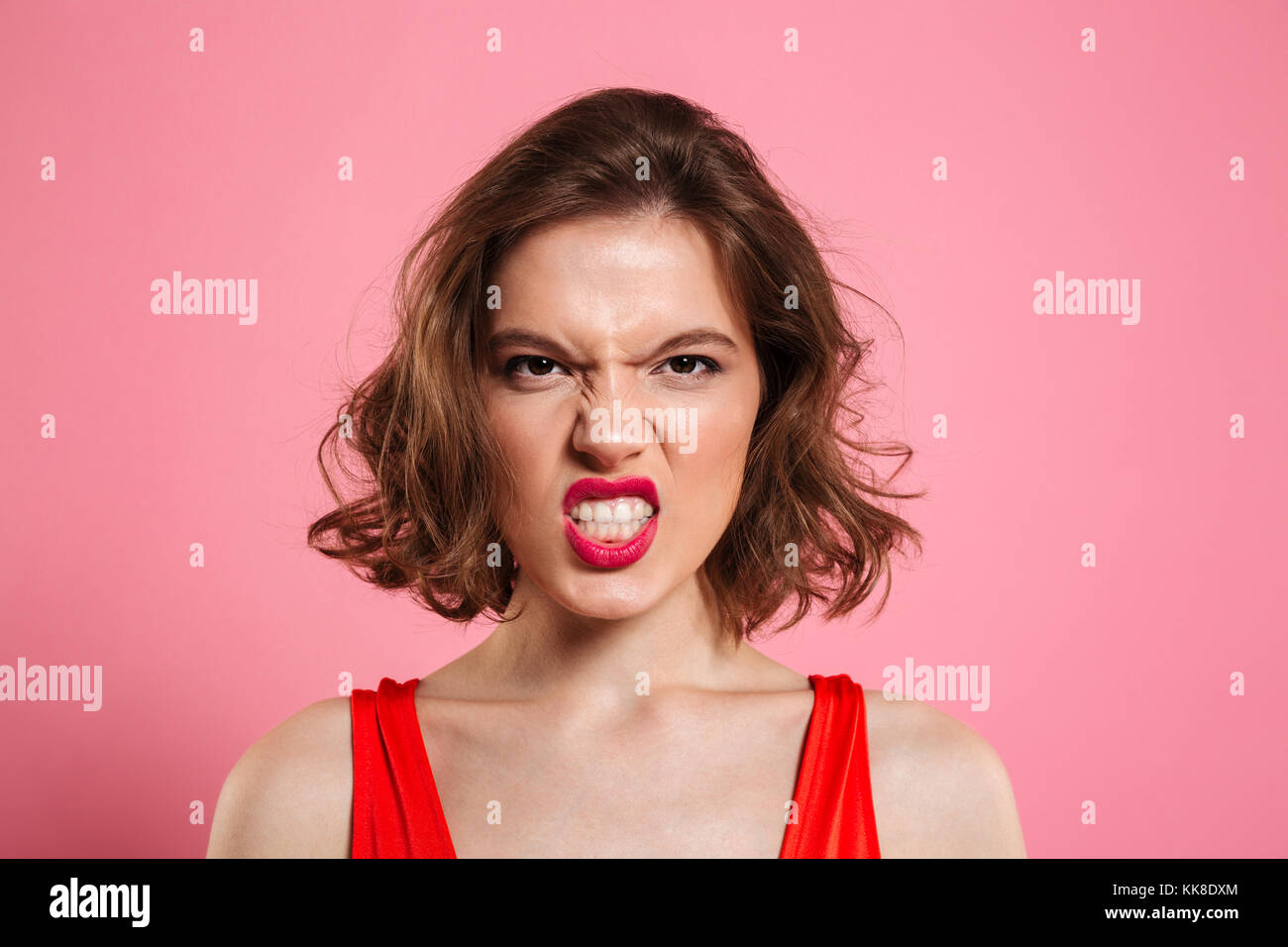 Close-up portrait of angry young woman with red lips looking at camera, isolé sur fond rose Banque D'Images