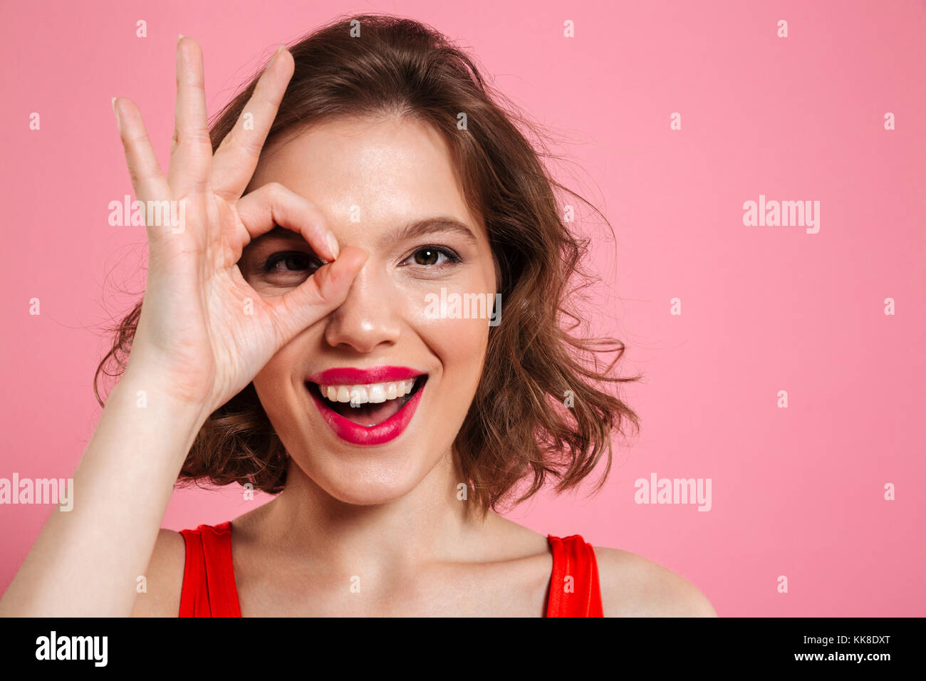 Close-up portrait of young happy girl with red lips looking at camera par OK sign, isolé sur fond rose Banque D'Images