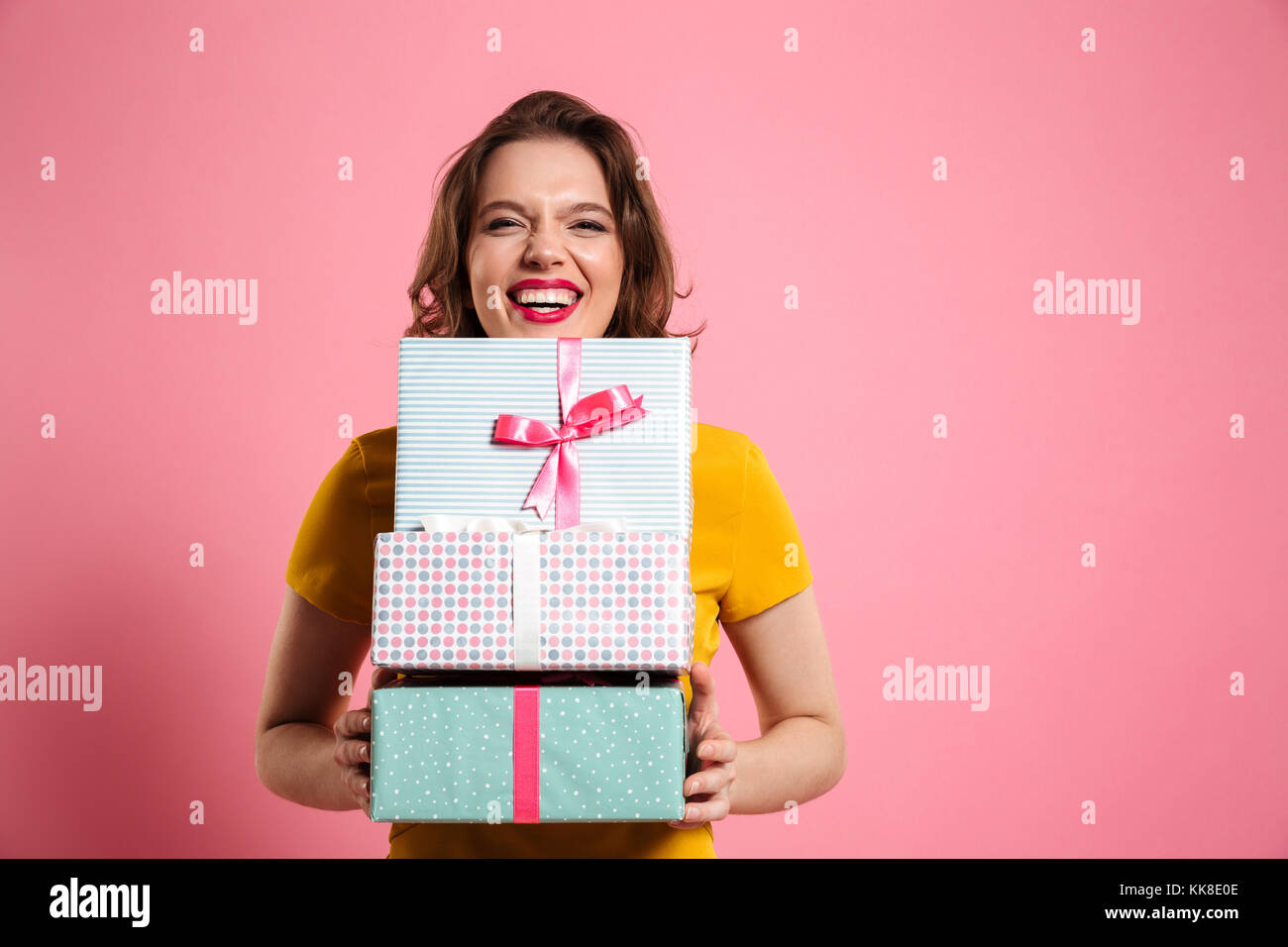 Happy laughing woman with red lips holding bunch of gift boxes, looking at camera, isolé sur fond rose Banque D'Images