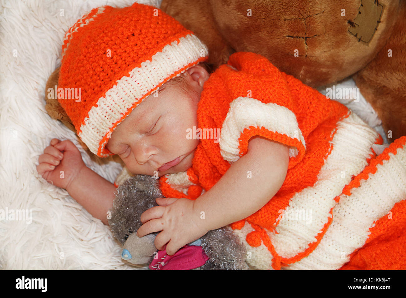 Portrait of cute bébé nouveau-né en costume orange dormir sur une couverture de fourrure blanche hugging ours en peluche. Banque D'Images